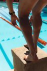 Sección baja de las piernas del nadador de pie en el bloque de partida en la piscina al aire libre en el día soleado - foto de stock