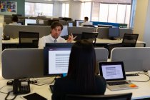 Vista trasera del ejecutivo femenino hablando con un colega masculino mientras trabaja en un escritorio en una oficina moderna - foto de stock
