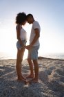 Vista lateral do casal afro-americano de humor romântico em pé na rocha perto do lado do mar. Eles estão cara a cara, de mãos dadas e olhando um para o outro — Fotografia de Stock