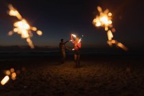 Front view of young couple playing with sparkler at beach. They are enjoying their holidays — Stock Photo