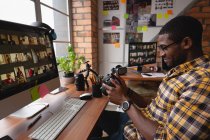 Боковой вид афроамериканского бизнесмена, улыбающегося и смотрящего на цифровую камеру в офисе — стоковое фото