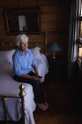 Високий кут зору вдумливої активної старшої жінки сидить на ліжку і тримає свій мобільний телефон в спальні вдома — стокове фото