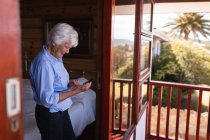 Seitenansicht einer glücklichen aktiven Seniorin, die ihr Mobiltelefon zu Hause im Schlafzimmer benutzt — Stockfoto