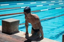 Front view of young Caucasian male swimmer getting out of outdoor swimming pool on sunny day — Stock Photo