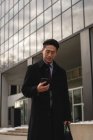 Vista frontal de jovens bem vestidos Empresário asiático olhando para o telefone celular enquanto caminhava na rua na cidade — Fotografia de Stock