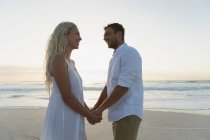 Vista lateral do jovem casal de amor de mãos dadas em pé na praia. Eles estão desfrutando suas férias — Fotografia de Stock