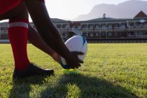Sezione bassa di un giocatore di rugby maschile che si prepara a calciare la palla nel terreno di rugby in una giornata di sole — Foto stock