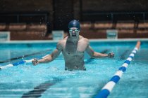 Vista frontale del giovane nuotatore maschio caucasico con le braccia tese a celebrare la vittoria nella piscina all'aperto sotto il sole — Foto stock