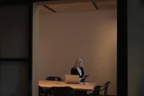Vorderansicht einer kaukasischen Geschäftsfrau, die ihr Smartphone benutzt, während sie im Büro im Konferenzraum sitzt — Stockfoto