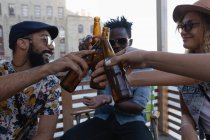 Vue de face du groupe d'amis divers trinquant avec des bouteilles de bière à la maison dans le balcon — Photo de stock