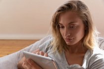 Вид спереду на молоду красиву жінку з використанням цифрового планшета вдома. Вона сидить на дивані — стокове фото