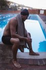 Vue latérale d'un homme nageur caucasien réfléchi assis sur le bloc de départ près de la piscine — Photo de stock