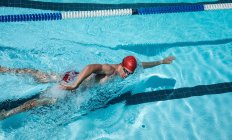 Vue en angle élevé du jeune nageur masculin caucasien nageant libre dans la piscine extérieure au soleil — Photo de stock