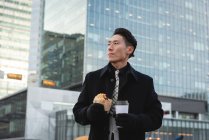 Front view of young Asian businessman thinking while standing on street in the city. Tenue de café et boulangerie — Photo de stock