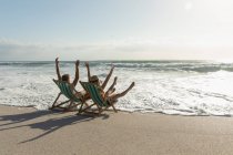 Rückansicht eines jungen Paares, das an einem sonnigen Tag auf einer Liege am Strand genießt. Sie genießen ihren Urlaub — Stockfoto