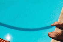 Vista de cerca de los pies descalzos del nadador masculino parado en la piscina al aire libre en un día soleado - foto de stock