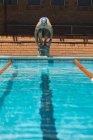 Vista frontal do jovem nadador caucasiano pronto para saltar para a água de uma piscina no dia ensolarado — Fotografia de Stock