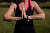Mittelteil einer aktiven Seniorin, die an einem sonnigen Tag Yoga macht und ihre Hände in den Park legt — Stockfoto