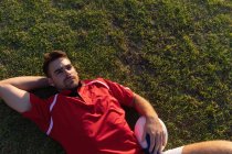 Vista ad alto angolo di un maschio sconvolto giocatore di rugby caucasico sdraiato con palla da rugby nello stadio — Foto stock