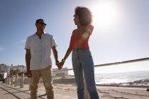 Низкий угол обзора афро-американской пары, стоящей и взаимодействующей друг с другом возле моря, держась за руки — стоковое фото
