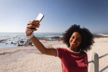 Vista frontal da mulher afro-americana tomando selfie na praia ao sol — Fotografia de Stock