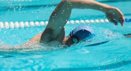 Close-up of young Caucasian male swimmer swimming freestyle in outdoor swimming pool on sunny day — Stock Photo