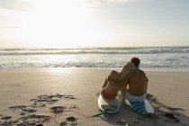 Visão traseira de casal feliz relaxando na prancha de surf na praia em um dia ensolarado. Estão a abraçar-se. — Fotografia de Stock