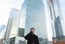 Низький кут зору молоді азіатські бізнесмена говорити на мобільний телефон, поки стоїть на вулиці в місті — стокове фото