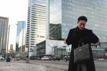 Низкий угол обзора молодой азиатский бизнесмен смотрит на смартфоны, разговаривая по мобильному телефону на улице в городе — стоковое фото