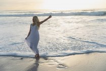 Vista frontal da bela mulher posando enquanto está de pé na praia em um dia ensolarado. Ela está feliz. — Fotografia de Stock