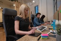 Низкий угол обзора довольно кавказская деловая женщина с помощью графического планшета, глядя на цифровой планшет с различными коллегами, работающих в офисе — стоковое фото