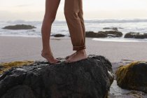 Низька секція молодої пари засмаглася стоячи на скелі на пляжі — стокове фото