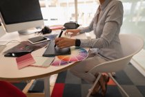 Seção baixa de uma designer gráfica feminina trabalhando sobre um tablet gráfico na mesa no escritório — Fotografia de Stock