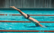 Seitenansicht einer jungen kaukasischen Schwimmerin, die an einem sonnigen Tag ins Wasser eines Swimmingpools springt — Stockfoto
