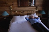Hochwinkelaufnahme einer aktiven Seniorin, die zu Hause im Schlafzimmer auf dem Bett schläft, die Hände hinter dem Kopf — Stockfoto