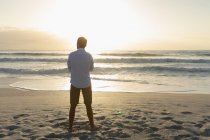 Rückansicht eines entspannten Mannes, der an einem sonnigen Tag am Strand steht. er beobachtet den Sonnenuntergang auf dem Ozean — Stockfoto