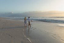 Rückansicht eines jungen Liebespaares, das sich an einem sonnigen Tag am Strand an der Hand hält — Stockfoto