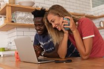 Seitenansicht eines multiethnischen Paares, das zu Hause über Laptop in der Küche steht und arbeitet — Stockfoto
