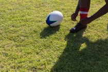 Angle bas d'un joueur de rugby masculin attachant ses lacets sur le terrain de rugby au soleil — Photo de stock