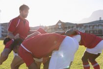 Vue latérale de joueurs de rugby multiethniques masculins se déplaçant comme un maul dans le stade par une journée ensoleillée — Photo de stock