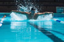Передній вигляд чоловічого плавця з плаваючим окуляром, що плаває метеликом у басейні — стокове фото