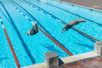 Vue grand angle des nageurs caucasiens hommes et femmes sautant dans l'eau en même temps à la piscine au soleil — Photo de stock