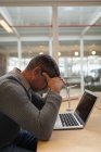 Seitenansicht eines traurigen Geschäftsmannes, der mit Laptop am Schreibtisch sitzt und den Kopf mit den Händen hält — Stockfoto