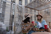 Angolo di vista basso di amici femminili multietnici che parlano tra loro mentre bevono bevande fredde in balcone — Foto stock