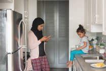 Seitenansicht einer Mutter mit gemischtem Geschlecht, die Hijab trägt, während sie zu Hause in der Küche steht — Stockfoto