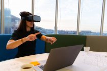 Vista frontal de la joven ejecutiva feliz usando auriculares de realidad virtual en una oficina moderna - foto de stock
