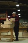 Vue de face du menuisier mesurant la planche de bois avec ruban à mesurer à l'atelier — Photo de stock
