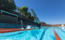 Vista de ángulo bajo de nadadores caucásicos masculinos y femeninos saltando al agua al mismo tiempo en la piscina bajo el sol - foto de stock
