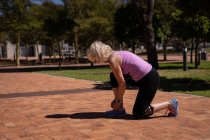 Seitenansicht einer aktiven Seniorin, die an einem sonnigen Tag ihre Schnürsenkel im Park bindet — Stockfoto