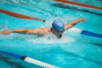 Vue de face du jeune nageur masculin caucasien travaillant dur tout en nageant course de papillon dans la piscine extérieure le jour ensoleillé — Photo de stock